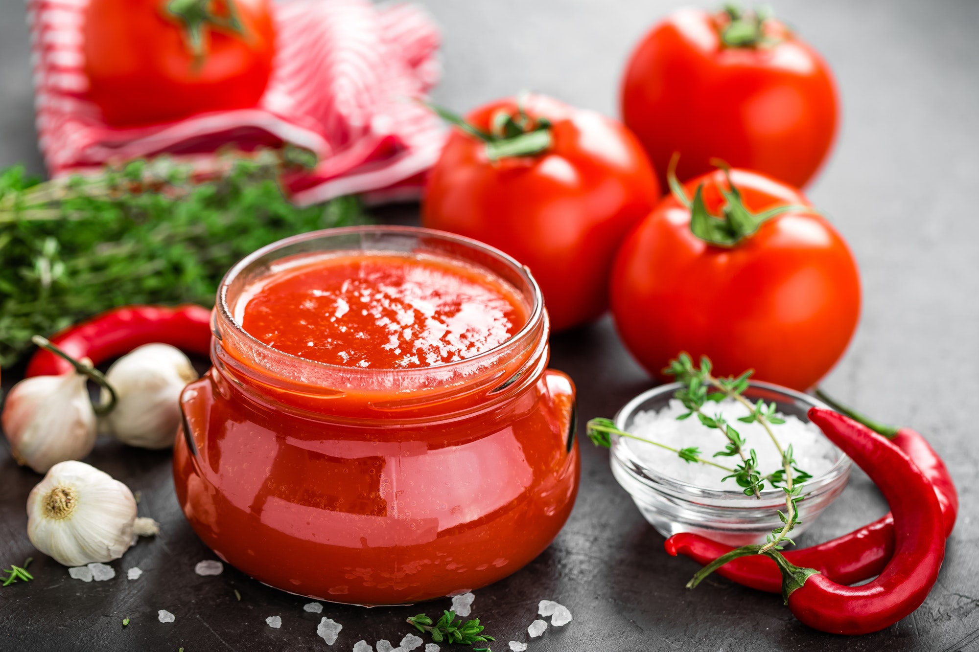 Tomato paste, puree in glass jar and fresh tomatos on dark background